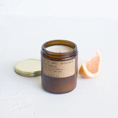 a grapefruit candle next to an orange slice on a white surface with a label