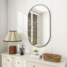 a white dresser topped with a mirror next to a lamp and a basket on top of it