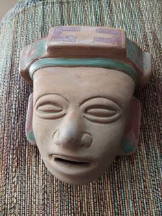 a clay mask is sitting on top of a woven tablecloth with an open mouth