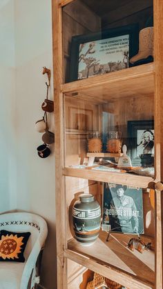 a wooden book shelf filled with books and knick - knacks next to a white chair