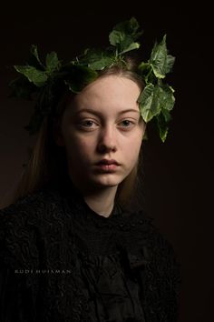 a woman with leaves on her head is posing for a photo in front of a dark background