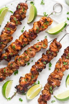 several skewers of meat with limes and cilantro on a white plate