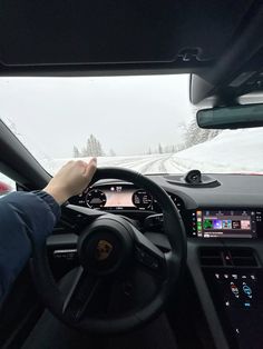 a person driving a car down a snow covered road with their hand on the steering wheel