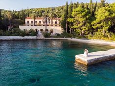 a large house sitting on top of a lake next to a lush green forest covered hillside