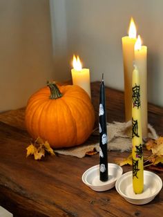 three candles with faces on them sitting on a table next to some leaves and pumpkins