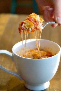 a person is taking a slice of pizza out of a white cup filled with soup