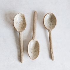 three wooden spoons with speckled paint on them are lined up against a white background