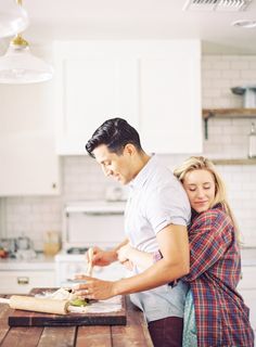 a man and woman are preparing food on a wooden table in the kitchen, one is holding his arm around the other's shoulder