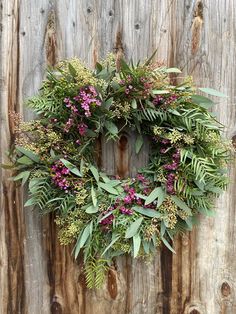 a wreath is hanging on the side of a wooden fence with purple flowers and green leaves