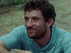 a close up of a person wearing a blue shirt and sitting in front of trees