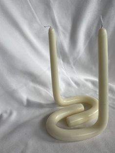 two white candles sitting next to each other on top of a white cloth covered surface