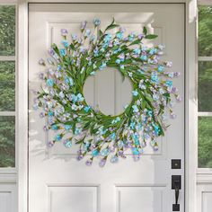 a wreath with blue flowers hanging on the front door to a white house in spring