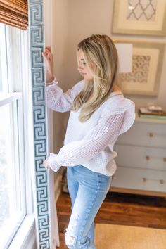 a woman standing next to a window with her hand on the side of the window