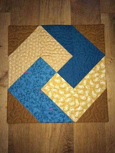 a blue and yellow patchwork quilt on a wooden floor with wood grains in the background