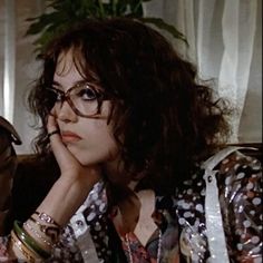 a woman with glasses sitting in front of a window next to a stuffed animal and potted plant