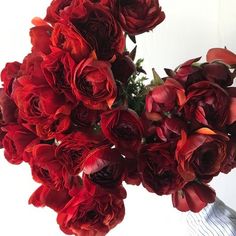 a vase filled with lots of red flowers on top of a white table next to a wall