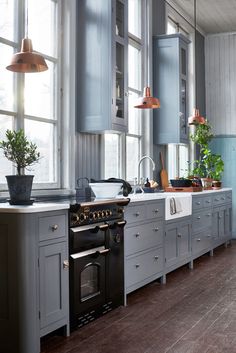 a kitchen with gray cabinets and an oven next to a window that has potted plants on it