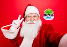 a man dressed as santa claus giving the peace sign with his hand while standing against a red background