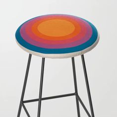 a stool with an orange, blue, and pink design on the seat is against a white background