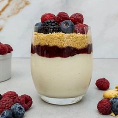 a dessert in a glass topped with berries and blueberries next to other food items