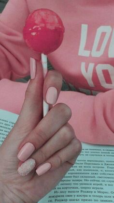 a woman is holding a lollipop in her hand and reading a book while wearing pink