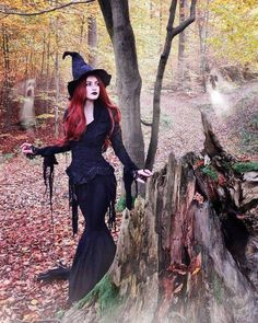 a woman dressed as a witch standing next to a tree stump