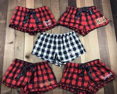 four pieces of red and black plaid shorts with monogrammed letters on them, sitting on a wooden floor