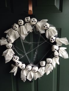 a wreath decorated with fake ghost heads and white paper bats is hanging on the front door