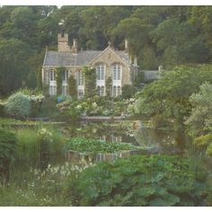 a large house surrounded by lush green trees and bushes next to a pond with water lilies