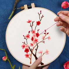 someone is working on an embroidery project with red flowers and branches in front of them