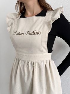 a woman wearing an apron with the name karem melatina on it, standing in front of a white wall