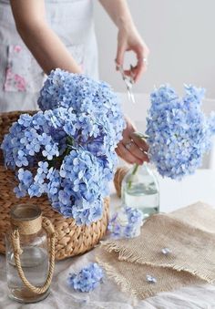 a woman is arranging blue flowers in a basket