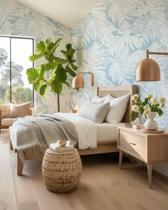 a bedroom with blue and white wallpaper has a bed, two nightstands, an end table, and a plant in the corner