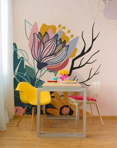 a dining table with two yellow chairs in front of a floral wall mural