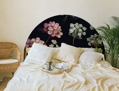 a bed with white linens and pink flowers on the headboard, next to a wicker chair