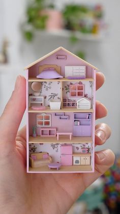 a hand holding a doll house made out of wood and pink paint on the inside