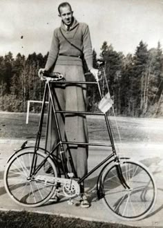 an old black and white photo of a woman standing next to a bicycle