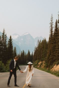 a man and woman holding hands while walking down the road