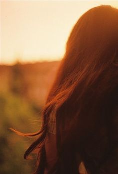 the back of a woman's head as she walks through an open field at sunset