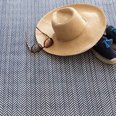 a pair of shoes and a straw hat on a blue carpeted area with herringbones