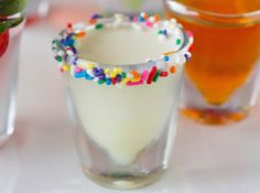 three shot glasses filled with liquid and sprinkles on a white plate next to strawberries