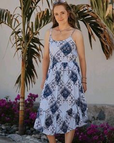 a woman standing in front of a palm tree wearing a blue and white patterned dress