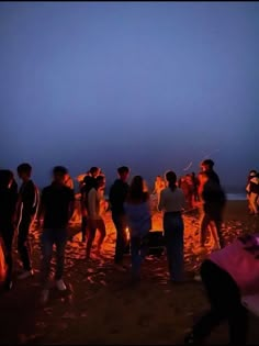 a group of people standing around a campfire on the beach at night with bright lights