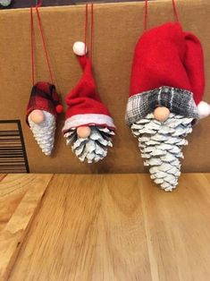 three christmas decorations are hanging on a wooden table, one is made out of pine cones and the other has an elf's hat