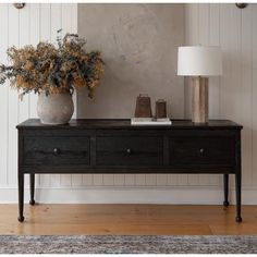 a black table with two vases on it and a lamp in the corner next to it