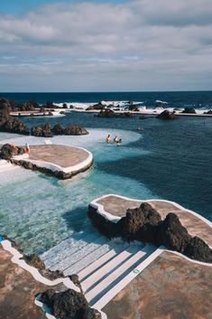 people are swimming in the ocean near some rocks