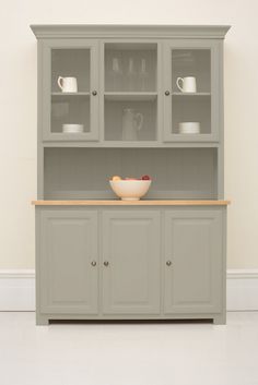 a white china cabinet with glass doors and dishes on the top, in front of a beige wall