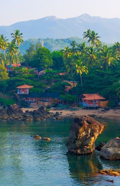 the beach is surrounded by palm trees and houses on top of rocks in the water