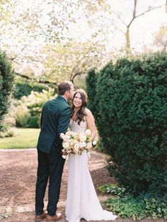 a bride and groom standing together in front of some bushes at the end of their wedding day