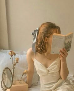 a woman reading a book while sitting on a bed with flowers in front of her